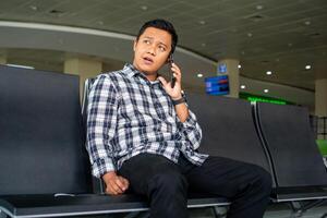 Asian man using mobile phone in airport waiting area. Male Tourist calling with his phone while waiting for departure in the airport. photo