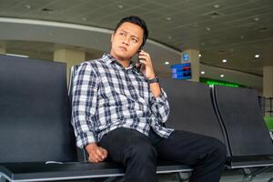 Asian man using mobile phone in airport waiting area. Male Tourist calling with his phone while waiting for departure in the airport. photo
