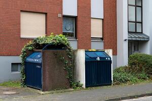 Two recycling bins covered in green foliage beside a building photo