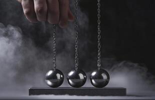 A hand is holding three balls that are suspended by chains. The balls are silver and appear to be in motion. photo