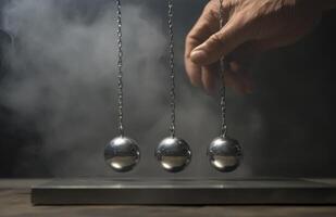A hand is holding three balls that are suspended by chains. The balls are silver and appear to be in motion. photo
