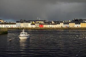 Cityscape sunrise scenery with old wooden boat in Corrib river at Claddagh in Galway city, Ireland, architecture background photo