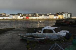 Cloudy cityscape sunrise scenery with old wooden boat in Corrib river at Claddagh in Galway city, Ireland, architecture background photo