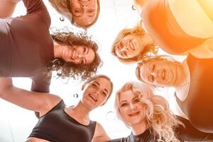 Low angle shot of smiling women looking at the camera, hugging, standing in a circle and doing team building photo