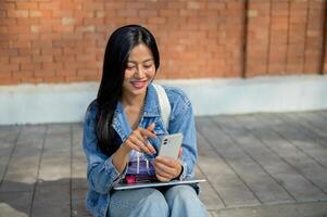 A female college student sits on the edge of a footpath at her university, using her smartphone. photo
