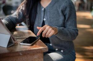 A cropped image of a woman using her smartphone while working remotely at an outdoor cafe table. photo
