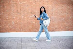 A side view of a smiling Asian female college student holding her smartphone while walking outdoors photo