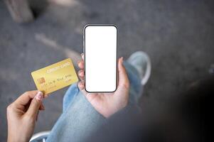 A top view of a woman sitting outdoors, holding a credit card and a smartphone with a screen mockup. photo