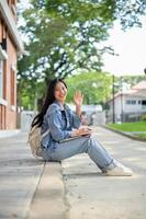 A student sits on the edge of a footpath in her university, waving and smiling at the camera. photo