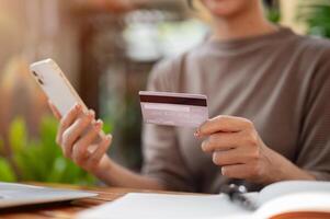 A woman holding a credit card and a smartphone while sitting at an outdoor table of a cafe. photo