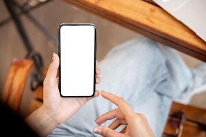 Awoman using her smartphone while sitting in a cafe. The smartphone with a white screen mockup. photo