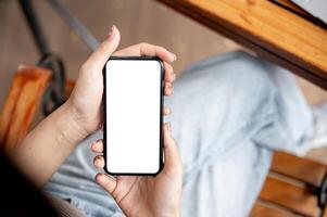 Awoman using her smartphone while sitting in a cafe. The smartphone with a white screen mockup. photo