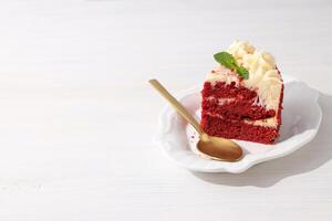 Piece of red velvet cake and spoon on plate on white wooden background, space for text photo