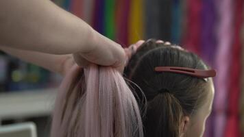 Close-up of hands weaving a pigtail for a child from a pink kanekalon. The concept of a master class on braiding kanekalon braids video