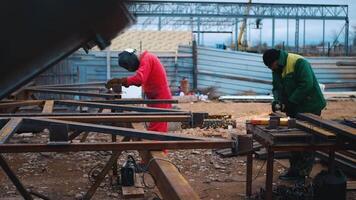 A mechanic in a construction uniform saws off metal structures with a grinder. Working on an industrial construction site video