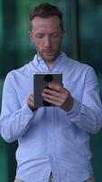 A Young Man Engaged in Using a Tablet While Outside with a Vibrant Urban Background video