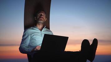 A Serene Evening Workspace A Man Reflecting Deeply with His Laptop Against a Beautiful Sunset video