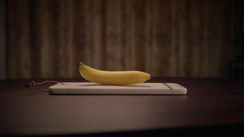 A bright yellow banana placed on a clean cutting board adorned with a rustic background video