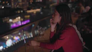 Night view of the city. A contemplative young woman enjoys the bright night view of the city from a rooftop bar. The soft glow of city lights creates a moody atmosphere. video