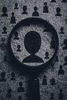 Magnified human icon silhouette under a magnifying glass on a black background with the shadow of many people icons, suggesting a hunting or employee selection concept. photo
