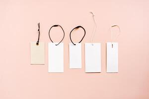Blank tags with different shapes and sizes are arranged in a row with string or cord attached, varying in color placed on a beige background photo