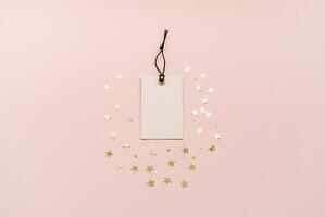 White tag with a black string is placed in the center, surrounded by gold star-shaped decorations on a soft beige background. photo
