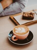 Cappuccino or latte with frothy foam in ceramic coffee cup and brownie cake on table photo
