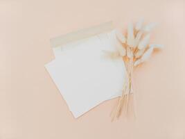 White blank card for text and envelope next to bouquet of dry Lagurus on beige background. photo