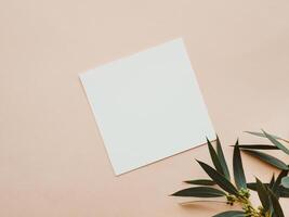 White blank paper square card mockup and green eucalyptus branch on beige background photo