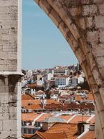 View of city buildings with tiled roofs in Lisbon through an archway in an ancient stone wal photo