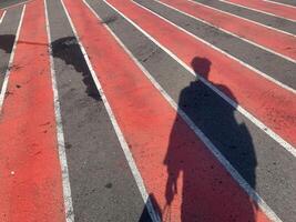 Silhouetted runner casts long shadow on vibrant running track. Athletic competition concept photo