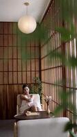 Young, caucasian woman enjoying a cup of coffee, tea lounge chilling near window in modern cozy apartment. Relaxed serene brunette girl feel fatigue lounge on comfortable sofa at home. video