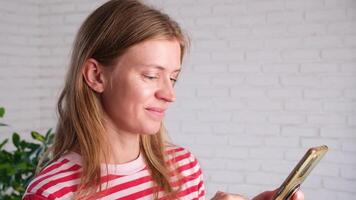 woman using smartphone at home with lots of plants, happily typing a message and looking photos video