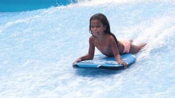 Little girl surfer balancing on a surfboard. Water sports activity. Child learning how to stand up on surfboard. The concept of practice and perseverance before it succeeds. Free copy space video