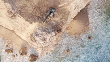 Escalators digging and destroying the rock on ocean coastline near Uluwatu temple. Drone top down view video