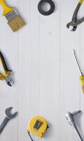 Top view flat lay of a workbench with tools like pliers, tape measure, screwdriver, and paintbrush, featuring a central empty space for promotional text photo