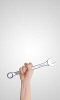Hand holding a wrench raised high against a gray background, vertical composition with free space for promotional text, ideal for tool branding or industrial concept photo