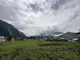 A view of a village in the mountains with a green field photo