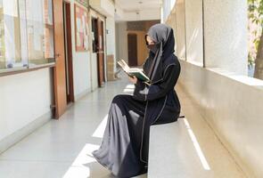 A beautiful Muslim students are intently reading Quran in the school building during breaks time in university with sun fare and blurred background. photo