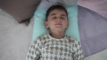 A little boy with short dark hair wakes up in the morning on the bed having a good mood. HD video