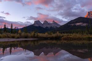 View of Three Sister Mountains, Canmore, Canada with Reflection in Lake at Sunrise photo