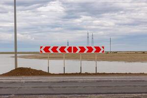 Road sign indicating a sharp curve near a waterlogged area on a cloudy day photo