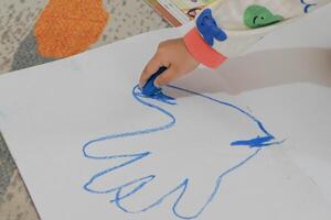 Child's hand drawing a hand with blue paint on paper photo