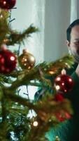 Man Smiles And Plays While Hanging Christmas Balls On Tree At Home video