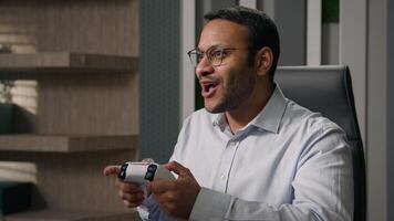 Funny lazy worker addicted game Indian man playing console controller play online at workplace in office afraid scared get caught Arabian businessman hide joystick pretend working with computer photo