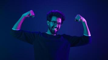 Funny Indian man slim guy fooling around show hands muscle biceps sport strong power bodybuilder ultraviolet neon studio background proud champion boast efficient security coding achievement level up photo