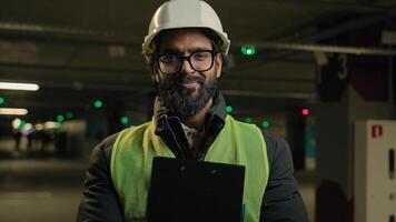 Indian contractor mechanic guy in helmet and glasses smile posing with clipboard folder. Arabian bearded man in eyeglasses worker male specialist manufacture work. Engineer in hard hat safety uniform photo