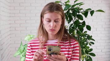 woman using smartphone at home with lots of plants, happily typing a message and looking photos video