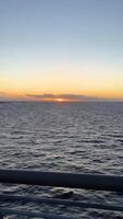 A breathtaking sunset captured as the sun dips below the horizon over the calm, expansive ocean. The golden rays stretch across the sea, casting a warm glow on the water's surface, while a few video