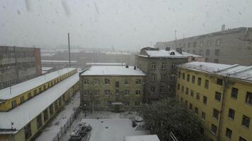 en lugn se av de först snö försiktigt beläggning hustak och gårdar av urban bostads- byggnader. fångad genom en fönster, de snöfall skapar en lugna och vintrig humör i sent höst video